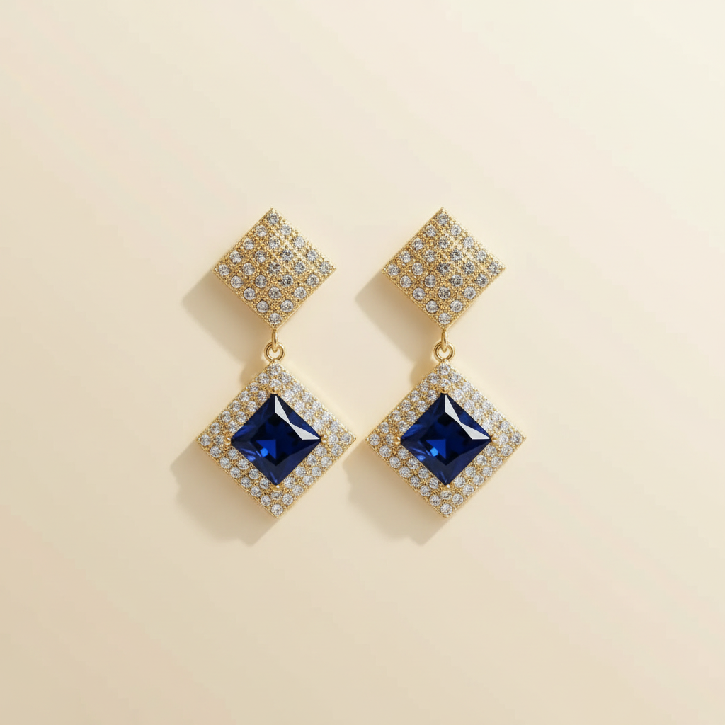 Gold-plated crystal drop earrings with deep-blue center stones on a warm ivory background