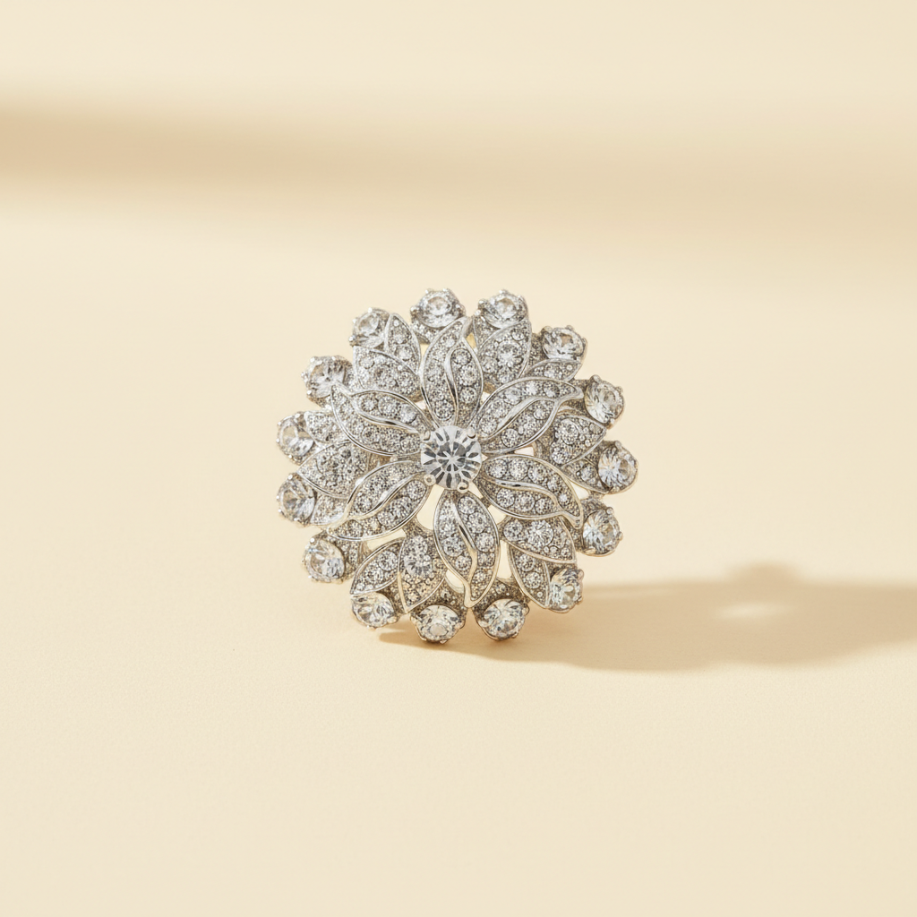 Silver-white leaf cluster brooch with clear glass stones on a warm ivory background