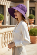 Woman wearing a purple wide-brim foldable sun hat on a sunlit terrace