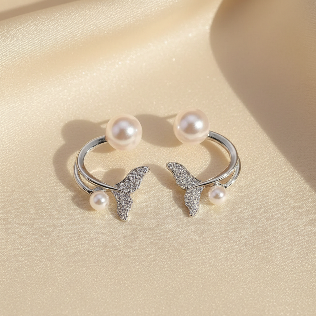 Silver fish tail stud earrings with pearl accents and pavé crystal tails on warm ivory silk