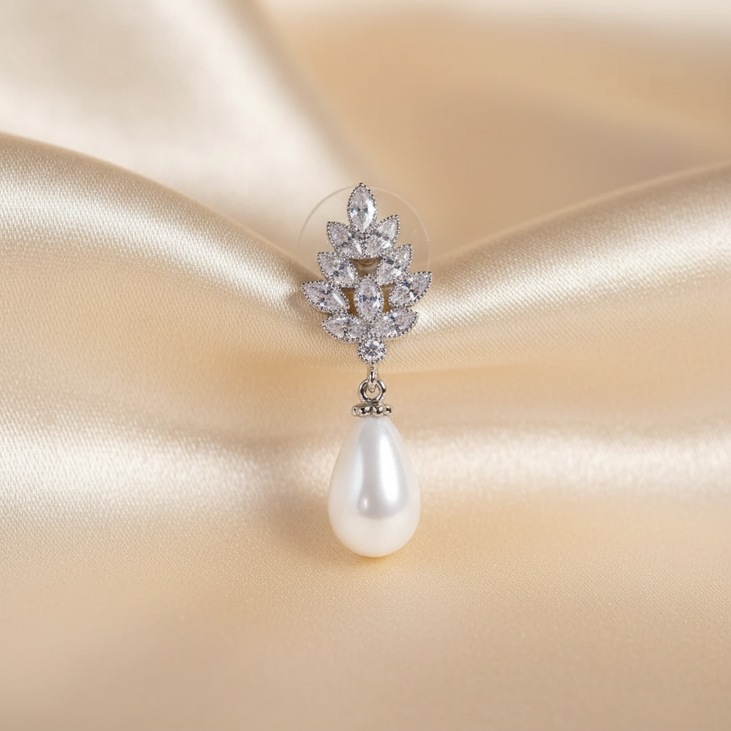 Close detail of a leaf-motif zircon pearl drop earring on ivory silk