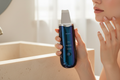 Woman holding a glossy black rechargeable facial skin scrubber beside a bathroom vanity