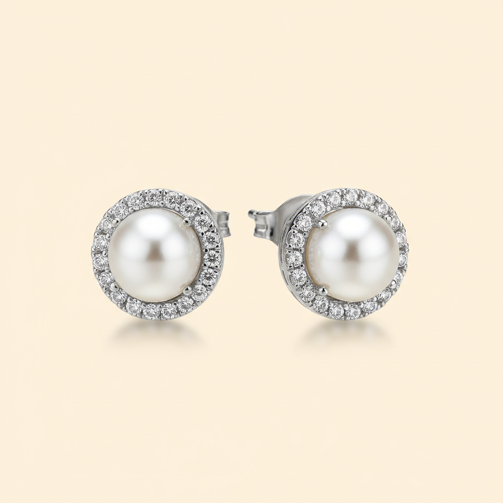 Pair of silver-plated imitation pearl and zircon stud earrings on a warm ivory background