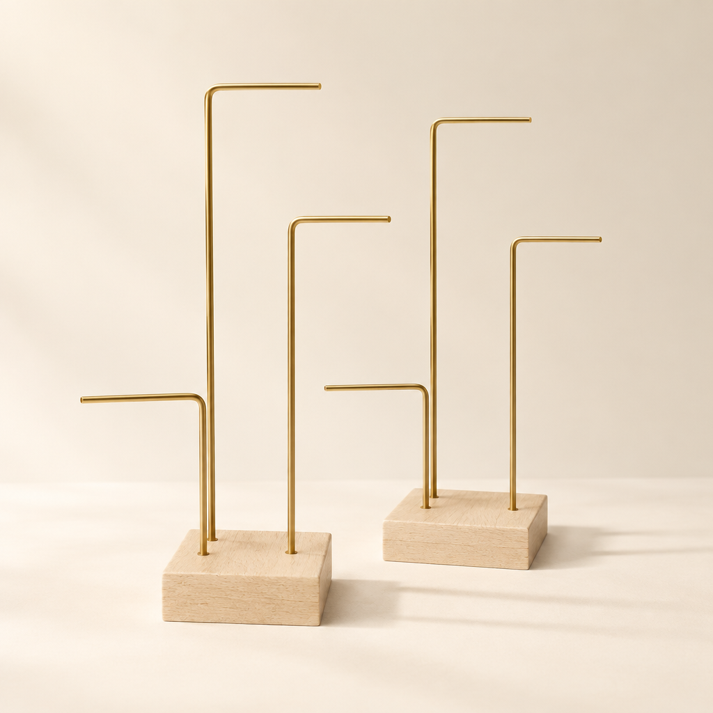 Two gold-tone metal jewelry display stands with pale wooden bases on an ivory background