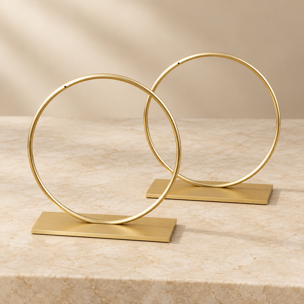 Two gold-plated circular metal jewelry stands with flat rectangular bases on warm ivory stone