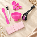 Pink facial skincare tool kit with bowl, spoons, stick, brush, dermaroller and headband on ivory background