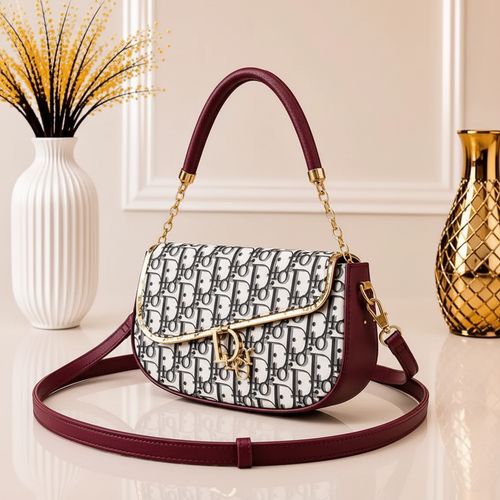 Close view of maroon leather shoulder bag with patterned body, gold-tone hardware and long strap