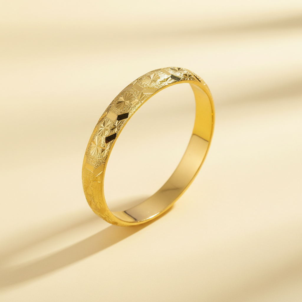 Engraved gold-tone bangle with geometric and starburst detailing on a warm ivory background