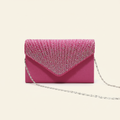 Pink satin envelope clutch bag with a pleated rhinestone flap and silver chain strap on a warm ivory background