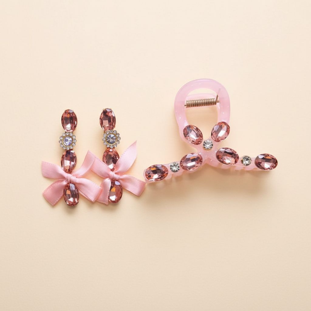 Pink embellished bow hair clip and matching drop earrings set on a warm ivory background