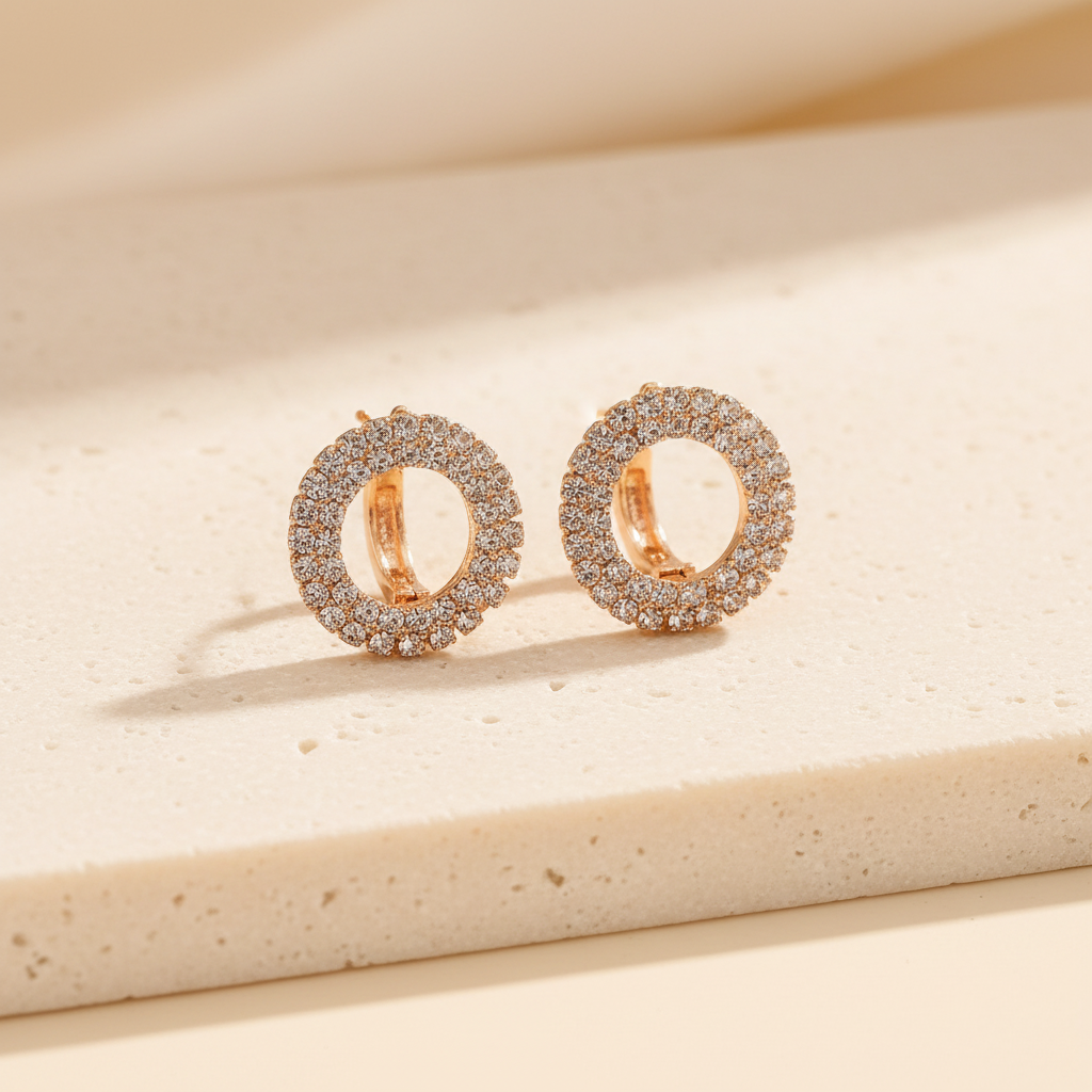 Pair of gold-tone round crystal earrings on a warm ivory stone surface