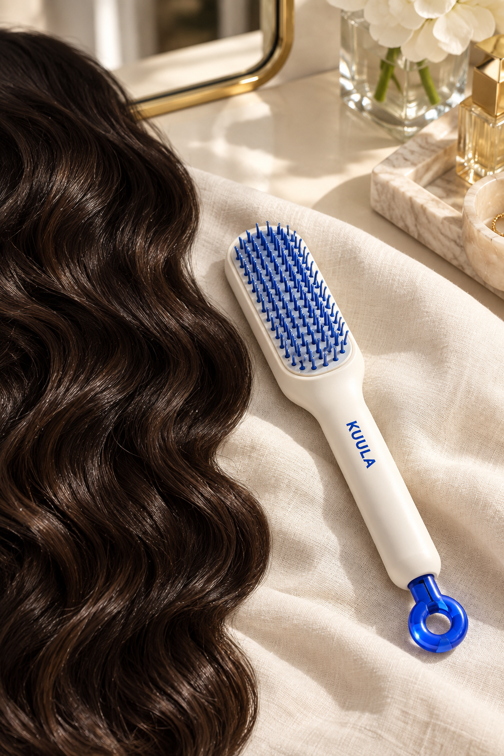 White and blue self-cleaning hair brush beside dark wavy hair on ivory linen
