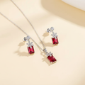 Silver-tone necklace with emerald-cut red zircon pendant and matching drop earrings on an ivory background