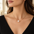 Gold-tone single pearl bead necklace worn with a black neckline