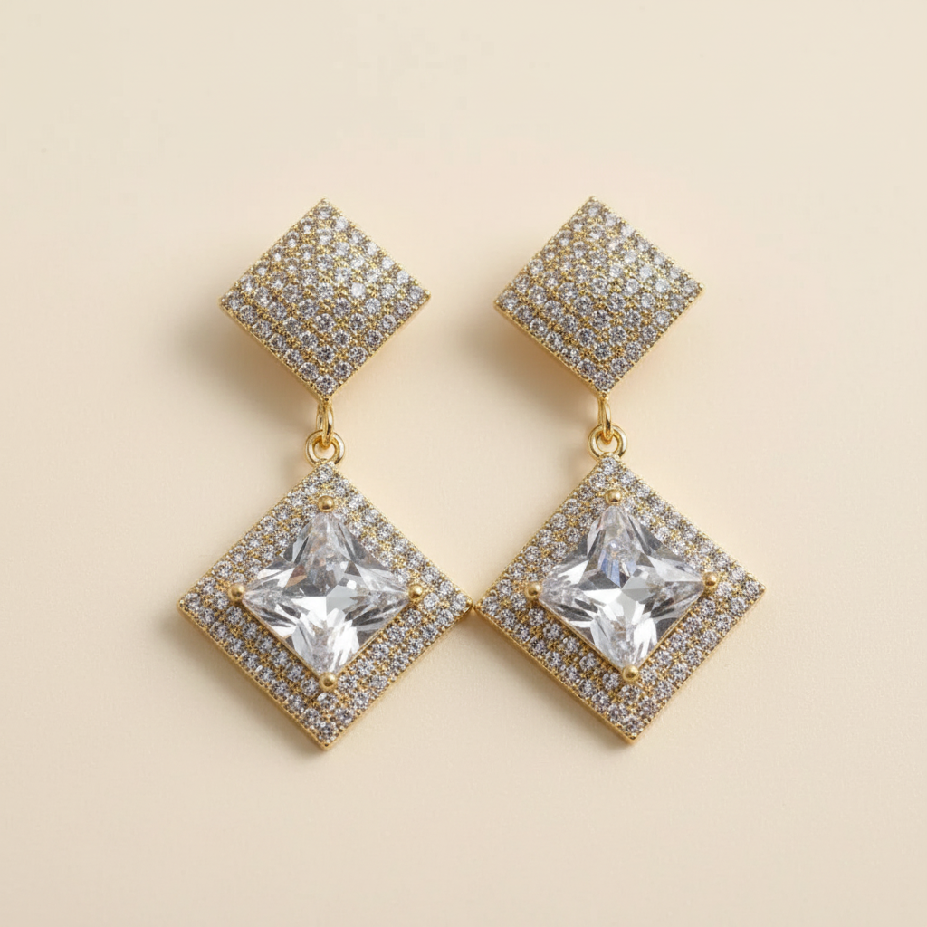 Close detail of gold-plated crystal geometric earrings on a warm ivory background