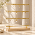 Gold three-tier earring organizer with wooden base holding earrings on a softly lit vanity