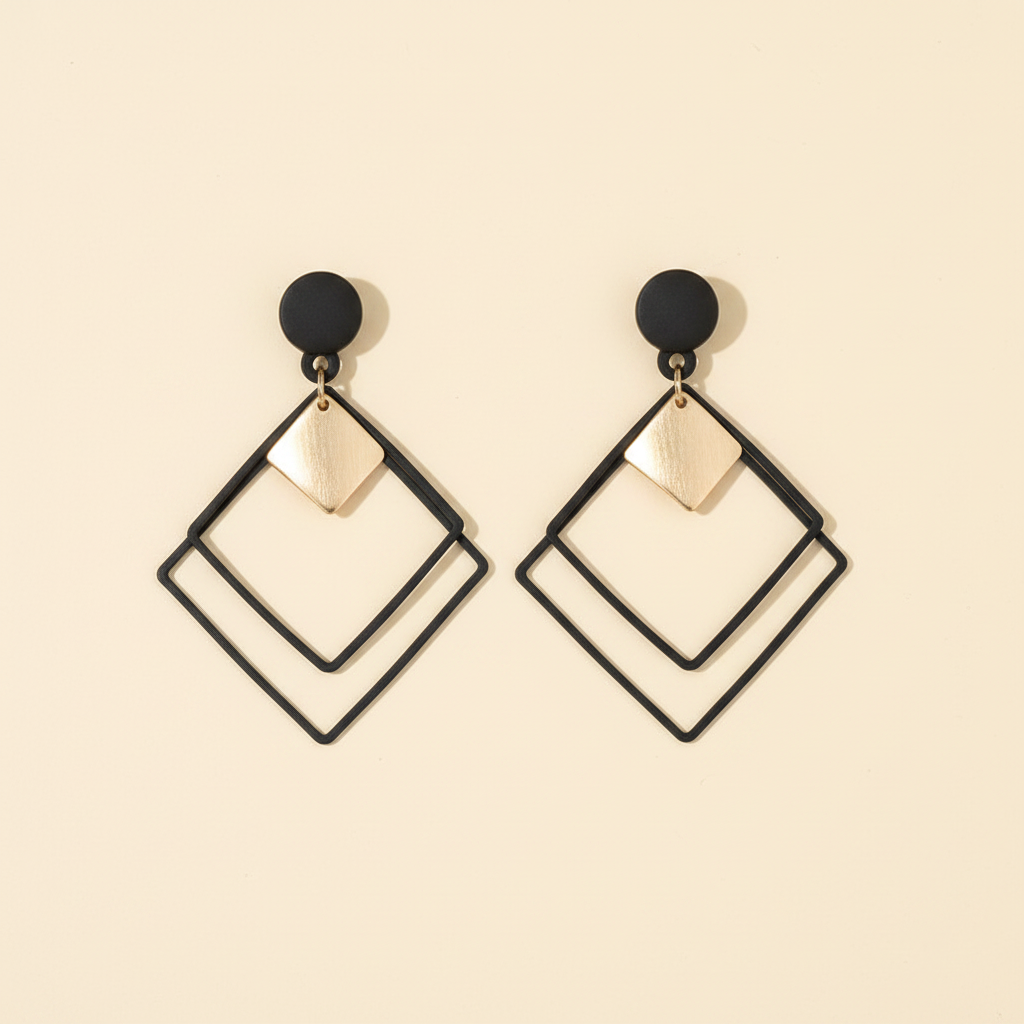 Pair of black and gold geometric square earrings on a warm ivory background