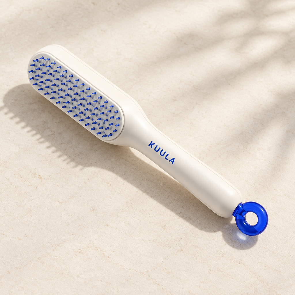 White self-cleaning paddle hair brush with blue bristles and blue handle-end mechanism on ivory surface