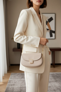 Woman wearing a beige leather shoulder bag with chain strap over an ivory tailored outfit