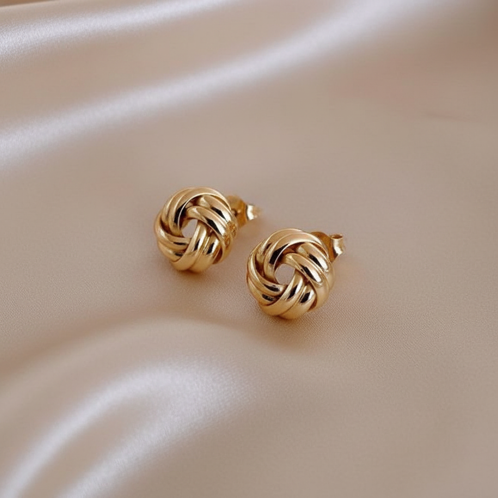 Close detail of gold-tone interlocking knot stud earrings on warm ivory fabric