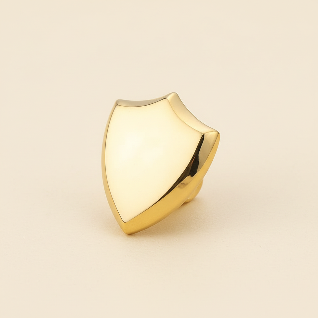Polished gold shield-shaped titanium steel pendant on a warm ivory background