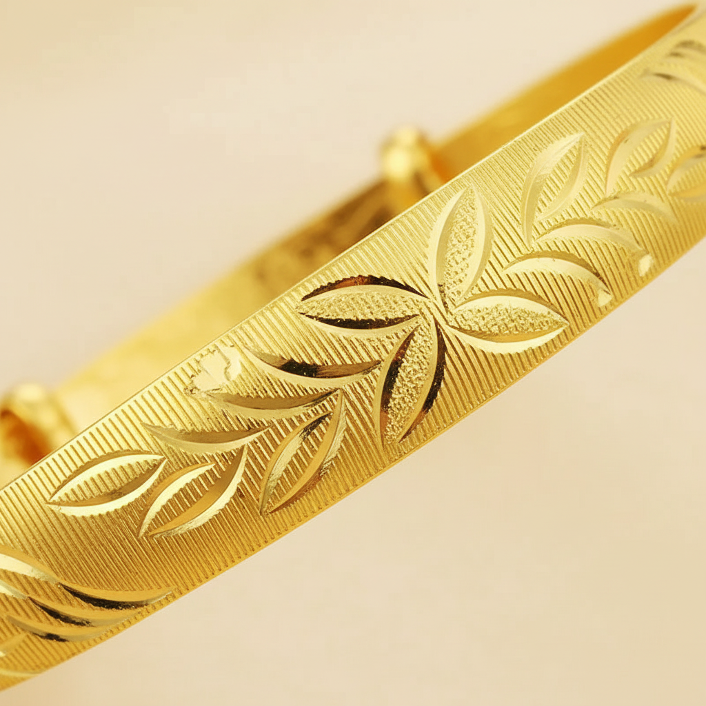 Macro detail of the gold-tone bangle’s leaf-and-floral engraving and push-pull closure