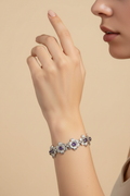 Silver-tone floral bracelet worn on a woman’s hand with purple stone accents