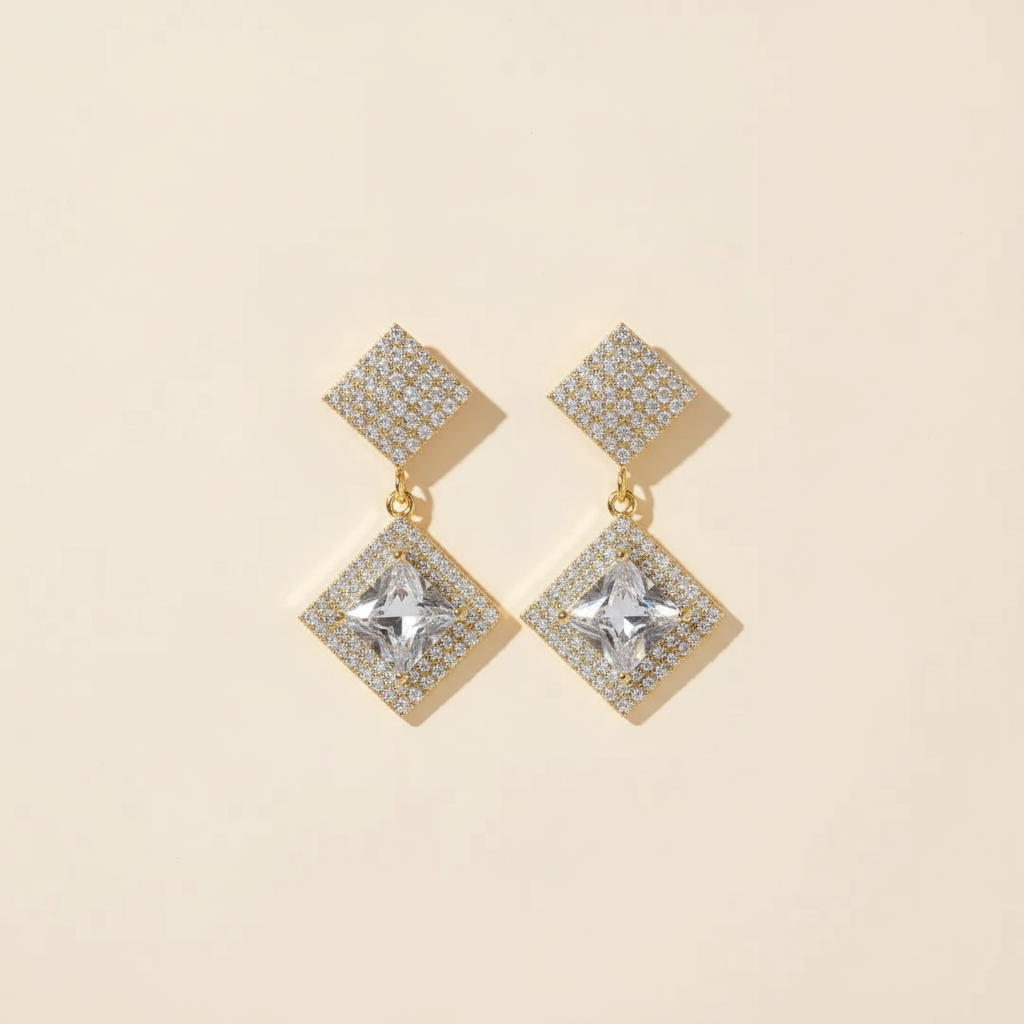 Gold-plated crystal geometric earrings arranged as a pair on a warm ivory background