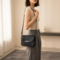Woman carrying a black leather shoulder bag with adjustable strap in a neutral interior